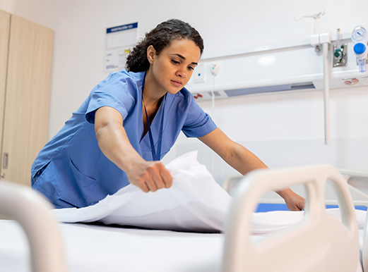 A worker, representing a Hispanic ALICE nurse, makes the bed in a hospital room.