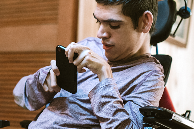 Young adult with a disability sitting in a wheelchair using his smartphone