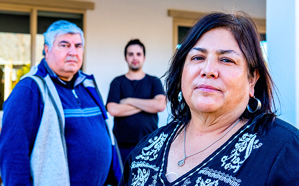 A mother, father, and teenager, representing a Hispanic ALICE family, stand staggered in the foreground and background with serious expressions.